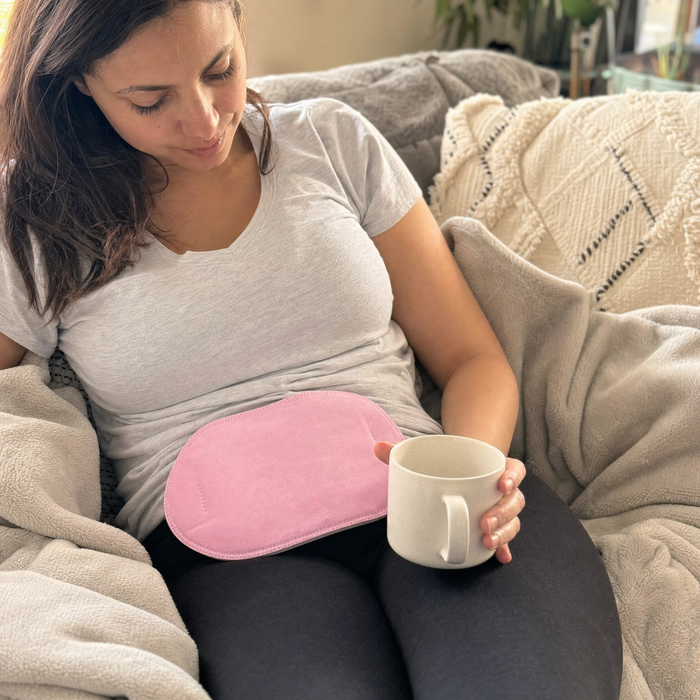 Woman curled on a couch with a HydroHeat steam wrap for period cramp relief