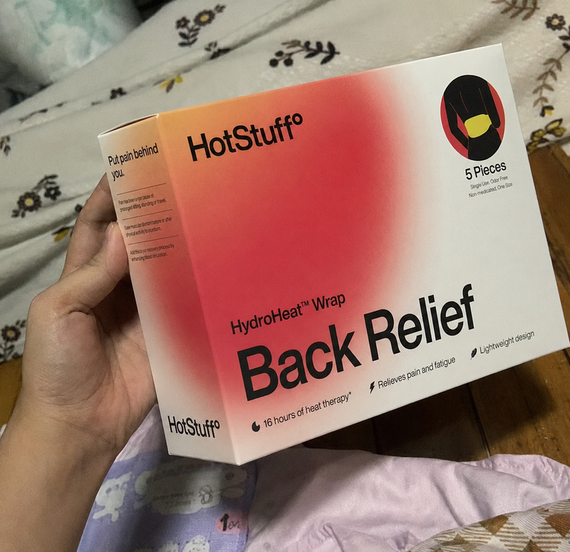 A hand holding the HotStuff Back Relief box above a bed